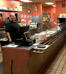Smiling adult poses behind the cafeteria cash register